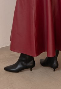 Röd midikjol i läder kombinerad med svarta läderstövletter med spetsig tå och en liten kitten heel, mot en neutral bakgrund.