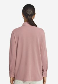 Långärmad, ljusrosa skjorta med krage, med knappade manschetter och en avslappnad passform, tillverkad av mjuk tyg. Bakifrån visad.