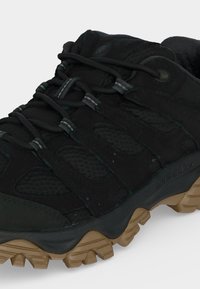 Chaussure de randonnée noire avec des panneaux en mesh, une semelle extérieure épaisse couleur bronzée et des lacets noirs passant dans plusieurs œillets.