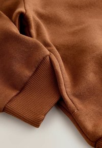 Brown sweatshirt fabric with ribbed cuffs, showing a textured surface and a soft, cozy finish. The cuffs are slightly fitted.