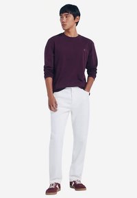 Dunkellila langärmeliges Hemd, weiße Hose und kastanienbraune Turnschuhe. Schlichtes Design mit Rundhalsausschnitt und minimalen Details. Glatte Textur durchgehend.