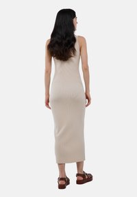 Robe maxi en tricot côtelé beige avec une silhouette ajustée, de larges bretelles et une texture lisse, associée à des sandales à plateforme marron.