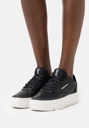 Black leather sneakers with a textured finish and thick white sole. Features include lace-up design and branded accents on the tongue and side.