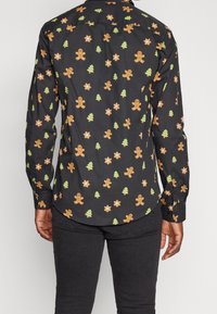 Camicia nera a maniche lunghe con bottoni, decorata con omini di pan di zenzero, alberi di Natale e motivi a stella in arancione e verde su uno sfondo scuro.