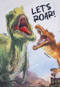 T-Shirt mit grafischen Dinosauriern: ein grüner T-Rex und ein orangefarbener Spinosaurus, beide brüllend vor einem weißen Hintergrund, mit dem Text "LASST UNS BRÜLLEN!"