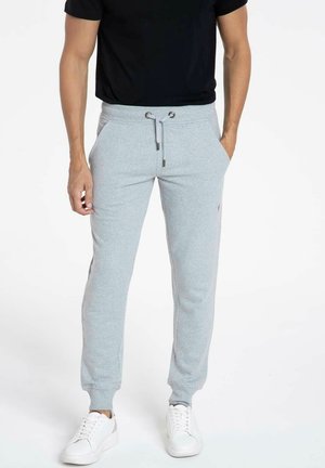 Pantalons de survêtement gris avec des poignets élastiques et une taille à cordon, associés à un T-shirt noir et des baskets blanches. Tissu doux, coupe décontractée.