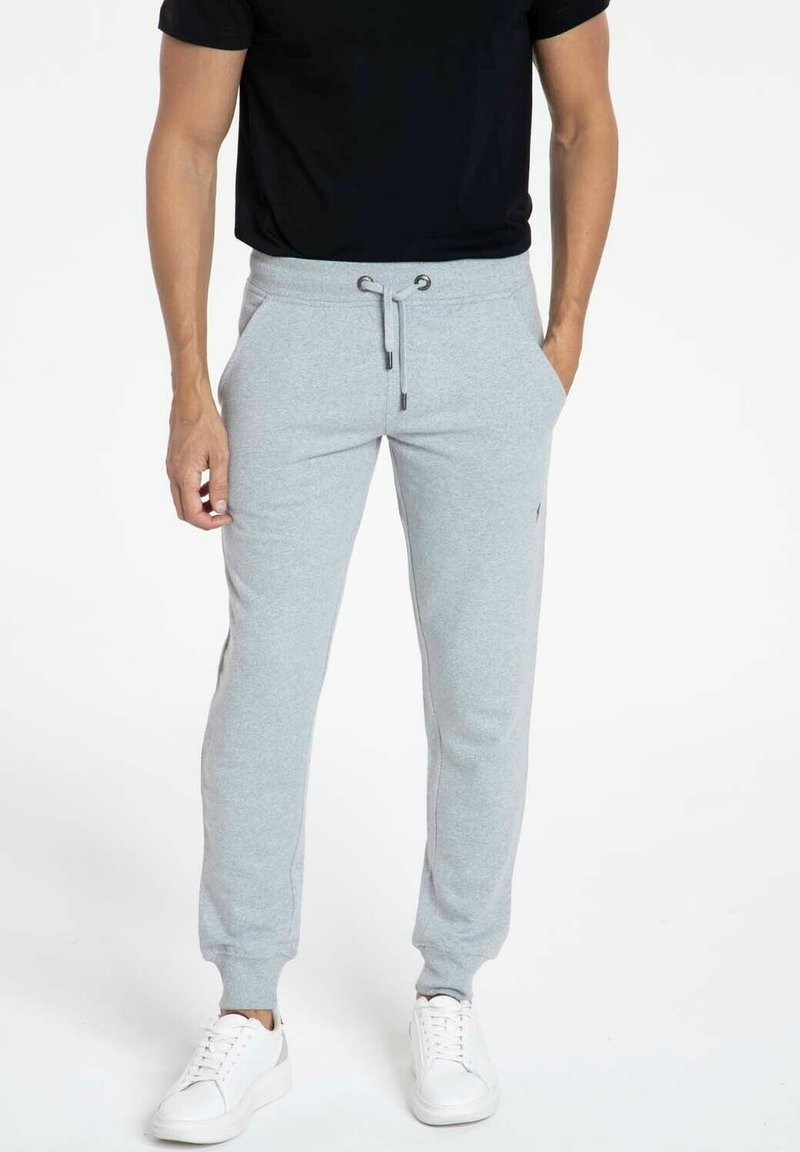 Pantalons de survêtement gris avec des poignets élastiques et une taille à cordon, associés à un T-shirt noir et des baskets blanches. Tissu doux, coupe décontractée.