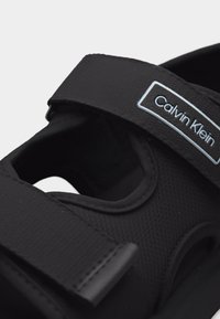 Μαύρο σανδάλι Calvin Klein με ρυθμιζόμενο λουράκι βέλκρο και επάνω μέρος από υφή υφάσματος.