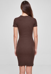 Robe brune ajustée en tissu côtelé, avec des manches courtes et un ourlet ondulé. Texture lisse, longueur mi-cuisse.