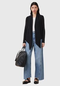 Black ribbed cardigan with an open front, paired with light blue wide-leg jeans. Holding a black leather tote bag and wearing black loafers.
