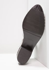 Suela de goma negra con un patrón texturizado y acentos de tachuelas plateadas. Diseño de punta afilada, talla 37, exhibiendo la marca "Bronx."