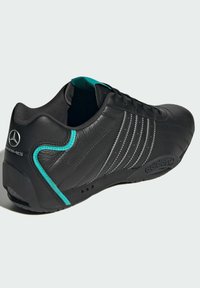 Black leather athletic shoe featuring three silver stripes, turquoise accents, and a textured sole with a logo on the heel.