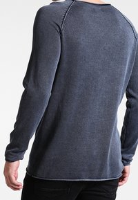 Mörkblå långärmad skjorta med ribbad textur, kontrasterande sömmar och rundad nederkant. Tyget är mjukt och har en avslappnad passform.