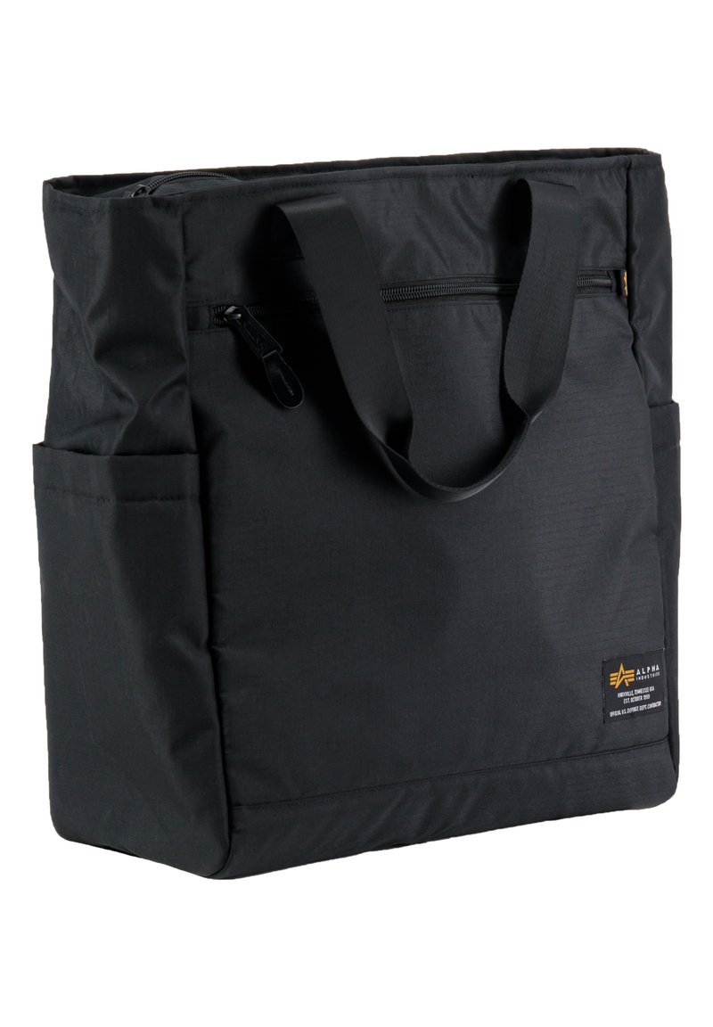 Bolsa de tela negra con cierre superior, doble asa y bolsillos laterales. Presenta un pequeño logo y una superficie texturizada.