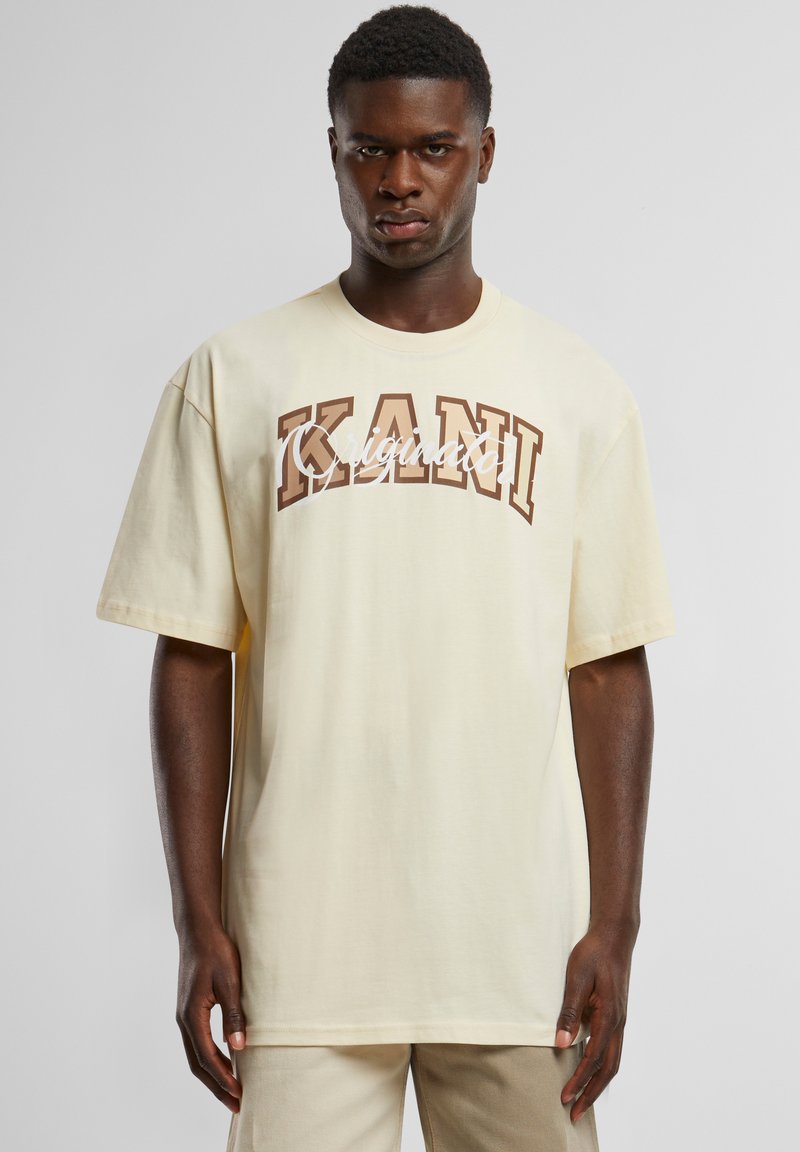 Cream cotton t-shirt with short sleeves featuring a large brown graphic text "KANI" and "Originato" in white cursive across the chest.