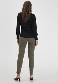 Black long-sleeve shirt paired with olive green fitted pants, with black heeled mules. Smooth fabric, simple design, and buttoned cuffs.
