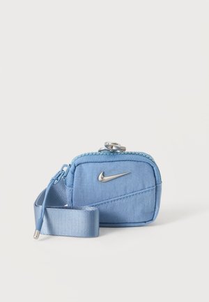 Малък светлосин ципен калъф със сребристо лого на Nike и прикрепена светлосиня каишка на бял фон.