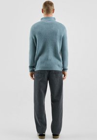 Jasnoniebieski sweter z dzianiny z wysokim kołnierzem, w połączeniu z luźnymi, ciemnoszarymi dżinsami i czarnymi butami, widziany od tyłu.