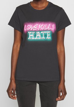 Osoba w czarnej koszulce z neonowym napisem na piersi "LOVE KILLS" różowym kolorem i "HATE" białym kolorem z turkusowym blaskiem.