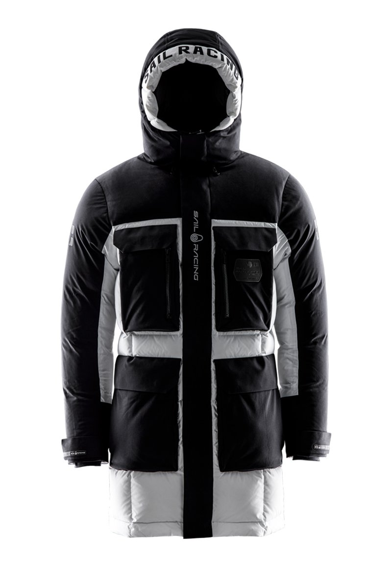 Vadderad parka med svart och vit färgsättning. Har dragkedja fram, stora fickor med dragkedja och en huva med varumärke. Slät textur.