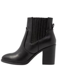 Bottine noire en cuir lisse, dotée d'un bout arrondi, d'un panneau élastique côtelé et d'un talon haut texturé.