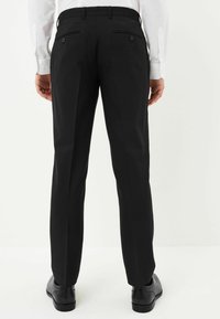 Schwarze maßgeschneiderte Hosen mit geradem Schnitt, ausgestattet mit hinteren Taschen mit Knöpfen. Der Stoff wirkt glatt und wird mit schwarzen Dressschuhen kombiniert.