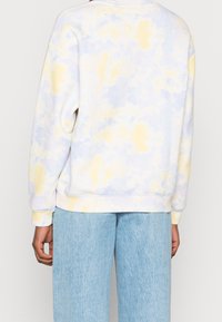 Sweatshirt tie-dye dans des couleurs pastel douces de jaune et de bleu, présentant une coupe décontractée, un col rond et des poignets côtelés avec une texture brossée.
