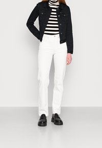 Black denim jacket, striped turtleneck, white straight-leg jeans, and black platform shoes. Clean lines, solid colors, and contrasting textures.