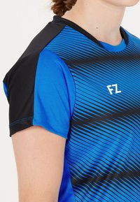 Blå atletisk tröja med svarta detaljer, med ett mönster av horisontella ränder, rund halsringning och korta ärmar. Logotypen "FZ" på bröstet.