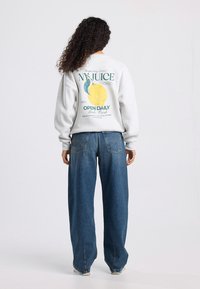 Gray sweatshirt with a graphic print featuring a yellow lemon and text on the back. Paired with loose-fitting dark blue denim jeans.