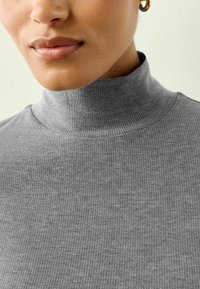 Grau gerippter Rollkragenpullover aus weichem Stoff, mit hohem Kragen und strukturiertem Muster. Keine sichtbaren Beschläge oder Akzente.