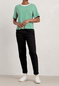 Randig t-shirt i grön och vit med rund halsringning, kombinerad med svarta byxor och vita sneakers, vilket visar en avslappnad passform.