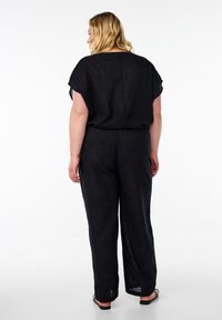 Salopette nera in lino con maniche corte, vestibilità rilassata, gambe larghe e una superficie leggermente texturizzata. Design minimalista senza chiusure visibili.