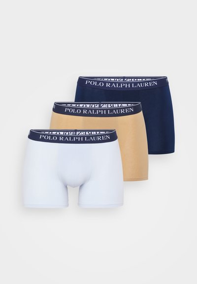 Três pares de boxers em branco, bege e marinho. Cada um tem uma cintura elástica de marca contrastante com a inscrição "POLO RALPH LAUREN".
