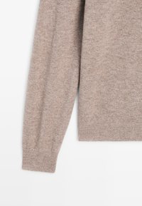 Beige sweater med en blød tekstur, rund halsudskæring og ribbede mansjetter. Har et enkelt design uden mønstre eller dekorationer.