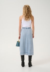 Heled sinine teksaseeliku maks püksiga, millel on veniv vöökoht, ja mustade saapadega. Käes on väike smaragdroheline käekott kollase aksendi jaotusega.