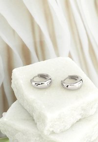 Silverringar med en polerad yta, med en böjd design och en sömlös låsning, placerade på vita kristallblock.