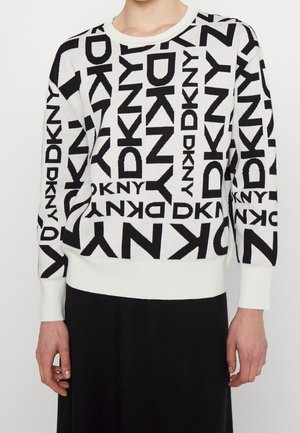 Suéter blanco con logotipos negros de "DKNY" repetidos en varios tamaños y orientaciones, combinado con una falda negra.