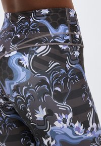 Κοντινή λήψη εμπριμέ κολάν με μπλε, μαύρα και λευκά αφηρημένα σχέδια λουλουδιών και κυμάτων στην περιοχή του ισχίου και της μέσης ενός ατόμου.