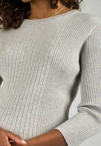 Pulover gri deschis din lână, cu guler rotund și mâneci trei sferturi. Textură moale a țesăturii, având modele verticale de dungi.
