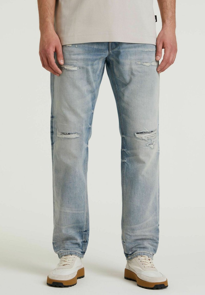 Lichtblauwe versleten denim jeans met een ontspannen pasvorm, voorzien van slijtage-details en vervaging. Gepaarde met witte sport schoenen.