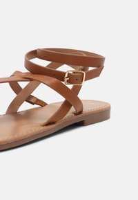 Ruske lamedanske sandale s križnim kožnim trakama i zlatnom kopčom. Glatki đon i minimalni detalji šivanja. Bez pete.