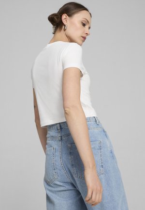 Top court à manches courtes blanc associé à un jean taille haute bleu clair. Présente un design simple sans motifs ni embellissements.