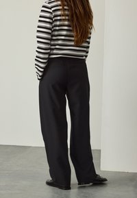 Pantaloni neri a gamba larga con una texture liscia, abbinati a una maglia a maniche lunghe a righe bianche e nere. Vista posteriore che mostra un design elegante.
