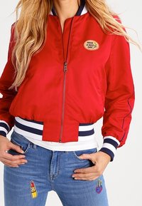 Czerwona bomberka z granatowymi paskami na kołnierzu i rękawach, z naszywką "MIŁEGO DNIA" oraz skróconym fasonem.