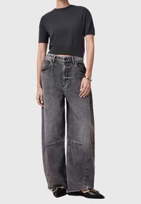 Grå croppad tröja med korta ärmar som matchas med vida, blekta grå jeans med fransade fållar och överdimensionerade fickor. Svarta slip-on-skor.