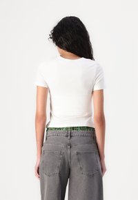 T-shirt bianco in cotone a maniche corte, con scollo rotondo, abbinata a pantaloni corti in denim grigi a vita alta e una cintura verde con motivo.