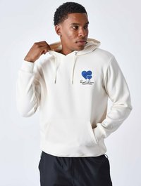 Hoodie crème avec une poche kangourou à l'avant, des cordons de serrage et un design de cœur bleu sur la poitrine. Le tissu semble doux et lisse.