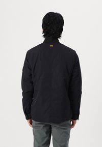 Black jacket with a solid design, high collar, and elastic cuffs. Features a small branded tag on the back and a smooth texture.