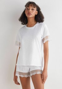 Witte katoenen slaapset bestaande uit een kortmouwtop met kantafwerking op de mouwen en bijpassende shorts met kantaccenten aan de zoom.